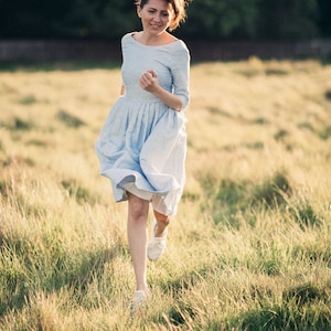 A smiling woman in a blue linen wedding dress runs through a vibrant field, radiating happiness and serenity.