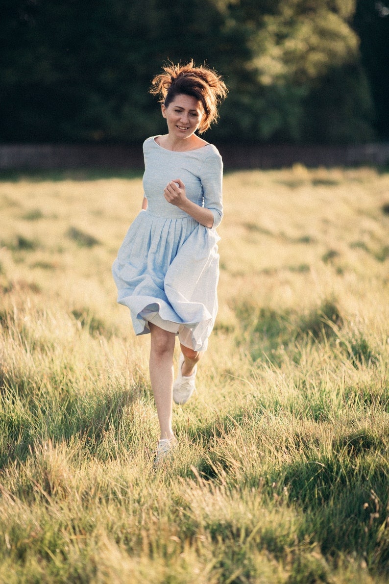 A smiling woman in a blue linen wedding dress runs through a vibrant field, radiating happiness and serenity.