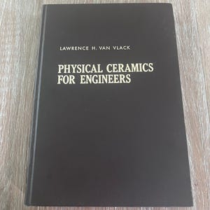 May include: A hardcover book titled Physical Ceramics for Engineers by Lawrence H. Van Vlack. The book features a solid black cover with the title and author name printed in a clean, white, sans-serif font centered on the front cover.