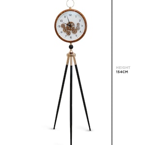Peut inclure: Une horloge de sol décorative avec un cadran rond et des engrenages apparents. Le cadran mesure 35 cm de diamètre et la hauteur totale est de 154 cm. Elle possède un trépied doré et noir et un cadre en bois.
