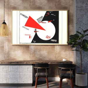 Può includere: Stampa artistica incorniciata con un audace design geometrico in rosso, nero e bianco. L'opera d'arte include testo russo e forme astratte, montata in una cornice di legno chiaro. La stampa è sopra una scrivania di legno.