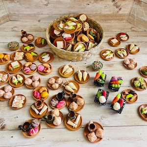 May include: A collection of miniature food items, including small plates of sandwiches, pastries, and vegetables, arranged on a light wood surface. A woven basket is filled with more miniature food items.