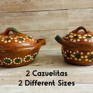 May include: Two brown cazuelitas, or small cooking pots, with lids. The pots are decorated with white and green floral patterns. The image includes the text "2 Cazuelitas 2 Different Sizes."
