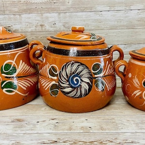 May include: Three terracotta cooking pots with lids. The pots are orange with black, white, green, and blue floral designs. Each pot has two handles. The pots are of varying sizes.