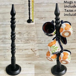 May include: A black wooden mug tree with a round base and a decorative top. The tree holds several ceramic mugs with orange floral designs. The text "Mugs not included" is visible.