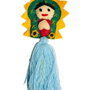 May include: A handmade felt ornament featuring a religious figure with a yellow halo and a light blue tassel. The figure has a black head covering, a beige face, and a red garment. The ornament is suspended by a red string.