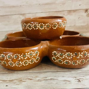 May include: A set of handcrafted, brown ceramic serving bowls. Each bowl is adorned with a repeating pattern of white and teal dots. The bowls are arranged in a unique, connected design, perfect for serving snacks or dips.