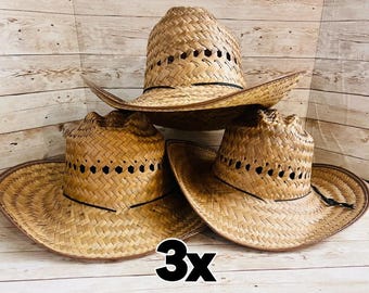 May include: Three straw cowboy hats with a woven design and a black band. The hats have a wide brim and a classic western style. The hats are made of a light brown material and are displayed against a light wood background.
