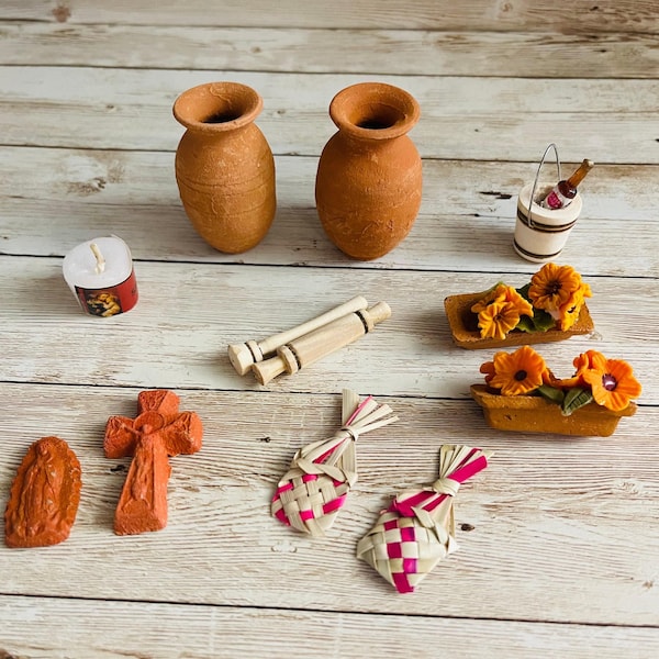 May include: A collection of miniature decorative items, including two terracotta vases, a candle, a cross, and two woven ornaments with pink accents. Also included are two small flower boxes with orange flowers and a miniature wine bucket.
