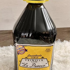 May include: A large, dark bottle of vanilla extract with a yellow label and a yellow handle. The label reads "Concentrated Flavor Vanilla L.T.M. La Pureza" and "Original Desde 1958". The bottle contains 4 liters.