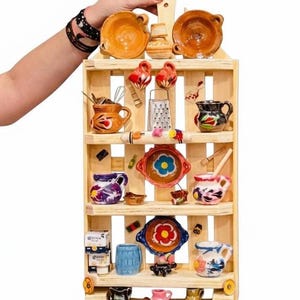 May include: A wooden shelf filled with miniature, colorful ceramic kitchenware. The shelf holds small bowls, cups, and decorative items. The items are painted with various designs and colors, including red, blue, and yellow. The shelf is held by a person.