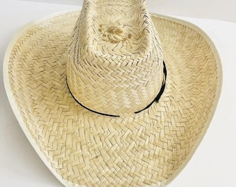 May include: A woven straw cowboy hat with a wide brim and a black band around the crown. The hat has a natural beige color with a white trim around the brim. The hat is designed to provide sun protection.