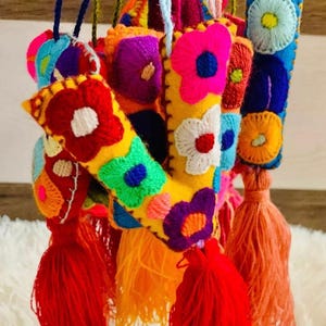May include: Close-up of colorful, embroidered felt ornaments with floral designs and tassels. The ornaments feature bright colors like red, yellow, blue, and purple. Each ornament has a tassel at the bottom. The ornaments are hanging.