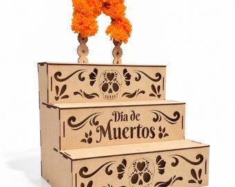 May include: A three-tiered wooden display stand featuring laser-cut skull motifs and the text "Día de Muertos" on the middle tier. The top tier is adorned with a decorative arch of bright orange artificial marigold flowers.