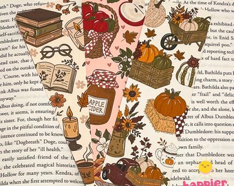May include: Three rectangular paper bookmarks featuring autumn-themed illustrations. The first shows books, glasses, and a candle. The second displays a basket of apples, a jar labeled Apple Cider, and leaves. The third depicts pumpkins, sunflowers, and a truck.