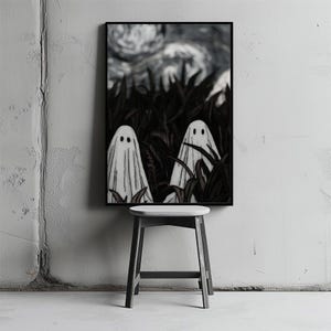 Puede incluir: Una impresión artística enmarcada que presenta dos figuras de fantasmas blancos con ojos negros, sobre un fondo oscuro y estilizado de follaje y un cielo nublado. La obra de arte se exhibe sobre un pequeño taburete de madera.