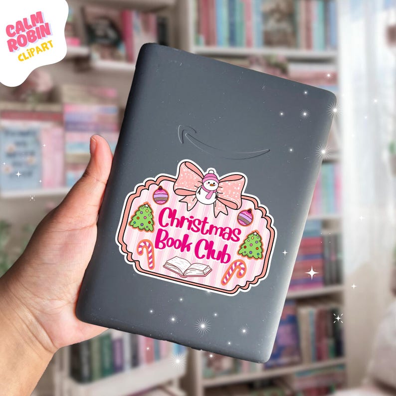 May include: A gray e-reader with a Christmas Book Club sticker. The sticker features a pink bow, snowman, Christmas trees, ornaments, and candy canes. The text "Christmas Book Club" is in pink and red.
