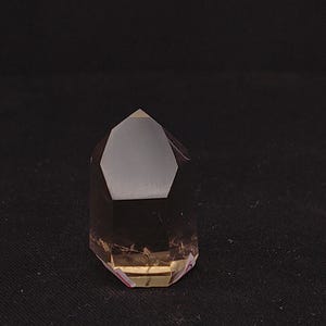 Può includere: Una punta di cristallo di quarzo fumé sfaccettata. Il cristallo è di colore marrone traslucido con una forma geometrica lucida. Il cristallo è posto su uno sfondo scuro.