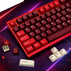 Op de afbeelding: Een rode mechanische toetsenbord met donkerrode keycaps. Het toetsenbord heeft een standaard QWERTY-indeling met witte en rode keycaps. Verschillende keycaps zijn losgemaakt, waaronder de Enter-toets en de WASD-toetsen.