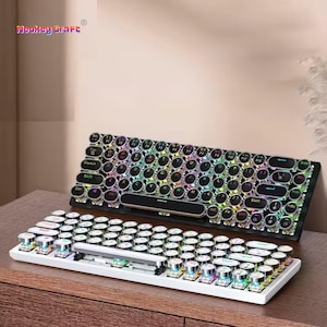 Może przedstawiać: Dwie klawiatury mechaniczne z okrągłymi nakładkami na klawisze. Jedna klawiatura jest biała, druga czarna. Obie klawiatury mają wielokolorowe podświetlenie LED. Tekst "Neokey Craft" znajduje się w lewym górnym rogu.