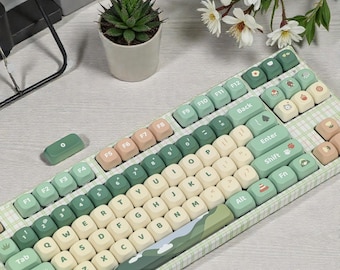 May include: A custom mechanical keyboard with a green and beige color scheme. The keycaps feature a variety of icons and illustrations. The keyboard has a plaid pattern and the brand name "Neokey Craft" is visible.