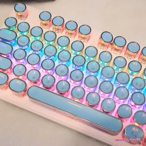 Könnte beinhalten: Eine hellrosa mechanische Tastatur mit hellblauen Tastenkappen. Die Tastenkappen haben weiße Buchstaben und Symbole. Die Tastatur hat eine hellblaue Leertaste und ist mit farbigen LED-Lichtern beleuchtet.