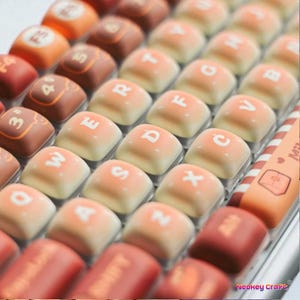 May include: Close-up of a keyboard with custom keycaps. The keycaps are in shades of orange, brown, and cream, with white lettering. Some keys have numbers and symbols. The keyboard has a unique design, with the text "Neokey Craft" visible.
