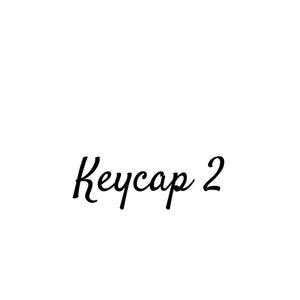 May include: A black text graphic on a plain white background that reads Keycap 2 in a cursive script font. The text is centered and features a stylized capital K followed by lowercase letters and the number 2 in a simple, clean typeface.