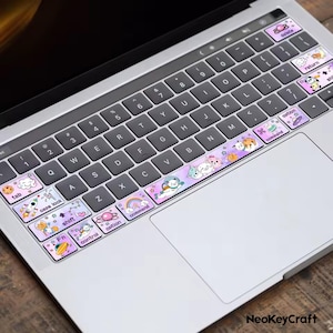 Peut inclure: Un clavier d'ordinateur portable avec des autocollants colorés représentant des animaux de dessins animés et des graphismes sur le thème de l'espace. Les autocollants sont placés sur les touches de fonction et la rangée inférieure du clavier. La marque "NeoKeyCraft" est visible.