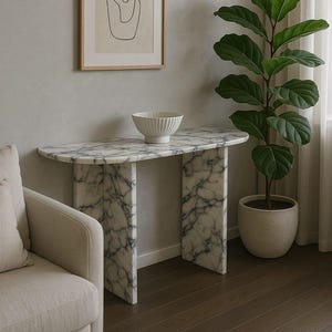 Puede incluir: Una consola de mármol con un patrón veteado blanco y gris. Un cuenco blanco está sobre la mesa. Una obra de arte abstracta enmarcada cuelga de la pared. Una planta en maceta con hojas verdes grandes está al lado de la mesa.