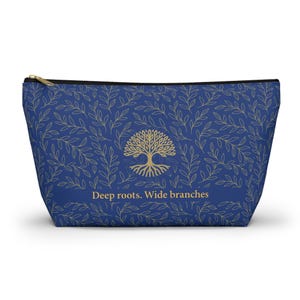 Puede incluir: Un neceser azul con un estampado de hojas doradas y un gráfico de árbol dorado. El neceser tiene una cremallera negra y el texto "Deep roots. Wide branches" en dorado.