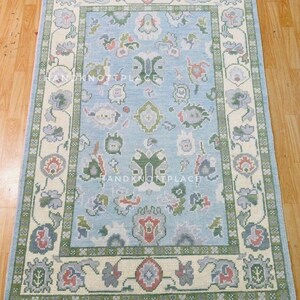 K&ouml;nnte beinhalten: Handgekn&uuml;pfter rechteckiger Teppich mit hellblauem Feld und cremefarbenem Rand. Der Teppich zeigt florale und geometrische Muster in Gr&uuml;n, Rot und Grau. Der Teppich ist aus Wolle und eignet sich f&uuml;r Wohn- oder Schlafzimmer.