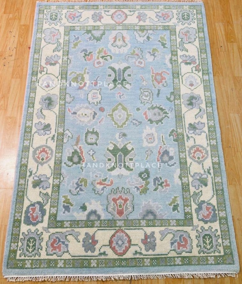 K&ouml;nnte beinhalten: Handgekn&uuml;pfter rechteckiger Teppich mit hellblauem Feld und cremefarbenem Rand. Der Teppich zeigt florale und geometrische Muster in Gr&uuml;n, Rot und Grau. Der Teppich ist aus Wolle und eignet sich f&uuml;r Wohn- oder Schlafzimmer.