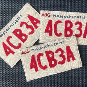 Puede incluir: Tres parches rectangulares de tela con un fondo beige claro y un sutil patrón de remolinos grises. Cada parche muestra el texto rojo bordado 4CB3A, con el texto azul AUG Massachusetts impreso sobre los caracteres rojos.