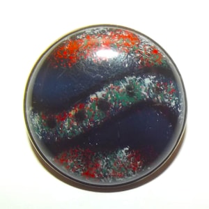 May include: A circular, polished stone with a dark blue base. It has bands of red, green, and white speckles, set in a gold-coloured metal. The design is symmetrical and the stone is round.