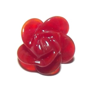 May include: A vibrant red, glass-like rose, with a glossy finish, sits against a white background. The flower's petals are tightly clustered, creating a detailed, three-dimensional effect. This decorative piece could be used as a pendant or a decorative element.