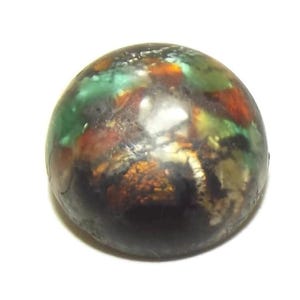 May include: A round, dark-colored object with a glossy finish. The surface displays a mix of colors, including green, red, and gold, creating a marbled effect. The object appears to be a decorative element or a small sculpture.