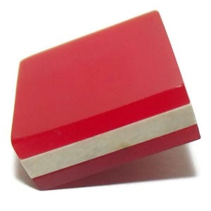 May include: A red, geometric-shaped object with a white and red stripe. The object has a glossy finish and is set against a white background. The shape is rectangular with angled sides.