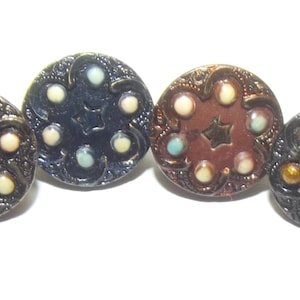 Puede incluir: Cuatro botones antiguos en varios colores: marrón oscuro, azul marino, cobre y marrón oscuro con detalles dorados. Cada botón presenta un diseño de estrella central rodeado de seis adornos circulares más pequeños.