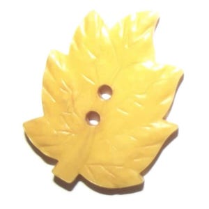 May include: A yellow leaf-shaped button with two holes for sewing. The button has a detailed leaf vein design and a slightly glossy finish. This decorative button is suitable for various sewing projects.