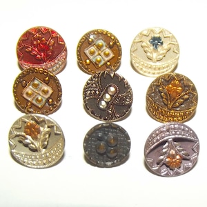 May include: A collection of nine circular buttons arranged in a grid. Each button features distinct metallic finishes, including red, bronze, gold, silver, and dark grey, with intricate embossed floral, geometric, and beaded patterns on their surfaces.