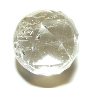 Può includere: Una sfera di cristallo trasparente e sfaccettata con inclusioni interne. La sfera è per lo più trasparente, con la luce che si riflette sulle sue numerose superfici. Il cristallo è posto su uno sfondo bianco, evidenziando la sua chiarezza e forma. L'aspetto generale è quello di una gemma lucidata.
