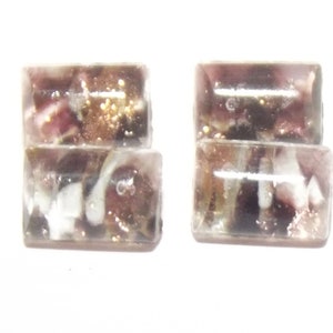 Puede incluir: Cuatro cuentas rectangulares de vidrio con una mezcla de colores, incluyendo tonos de morado, marrón, blanco y dorado. Las cuentas están apiladas en pares, con un acabado transparente y brillante. Las cuentas son probablemente para hacer joyas.