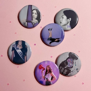 May include: A collection of six round pinback buttons featuring images of a female celebrity. The buttons have various images, including a woman holding a megaphone, and a woman with the word "Obsessed" on a sash.