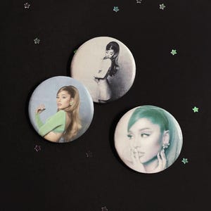 May include: Three circular pin-back buttons featuring photographic portraits of a person with long hair. One button shows a person in a green top, another shows a person in a light-colored dress, and the third shows a close-up portrait of a face.