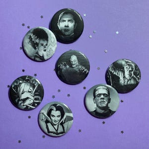May include: A collection of seven black and white pinback buttons featuring classic monster movie characters. The buttons are round and vary in size, with images of Frankenstein's monster, the Bride of Frankenstein, and Dracula.