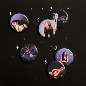 May include: Six circular pin-back buttons featuring photographic prints of a person. Button 1 shows a person resting their head on a hand. Button 2 says bad idea right. Button 3 says GUTS with stars. Button 4 shows a person sitting. Button 5 shows a person lying down. Button 6 shows a person gesturing.