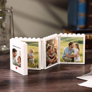 May include: A white, modular, brick-style folding picture frame featuring three connected panels. The frame displays photographs of a family in a grassy field. The front panel includes the text "Williams, Jason" and a small red heart icon.