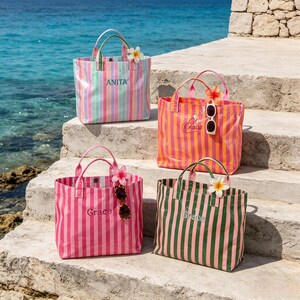 May include: Four rectangular tote bags with vertical stripes in various color combinations. Each bag features two top handles, a personalized name embroidered on the front, and a decorative flower accessory attached to one handle.
