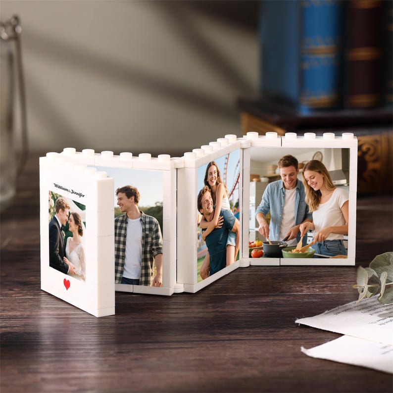 May include: A white, interlocking plastic brick photo frame featuring four connected panels. The first panel displays the text "Williams & Jennifer" above a red heart. Each panel holds a different photograph of a couple in various settings.